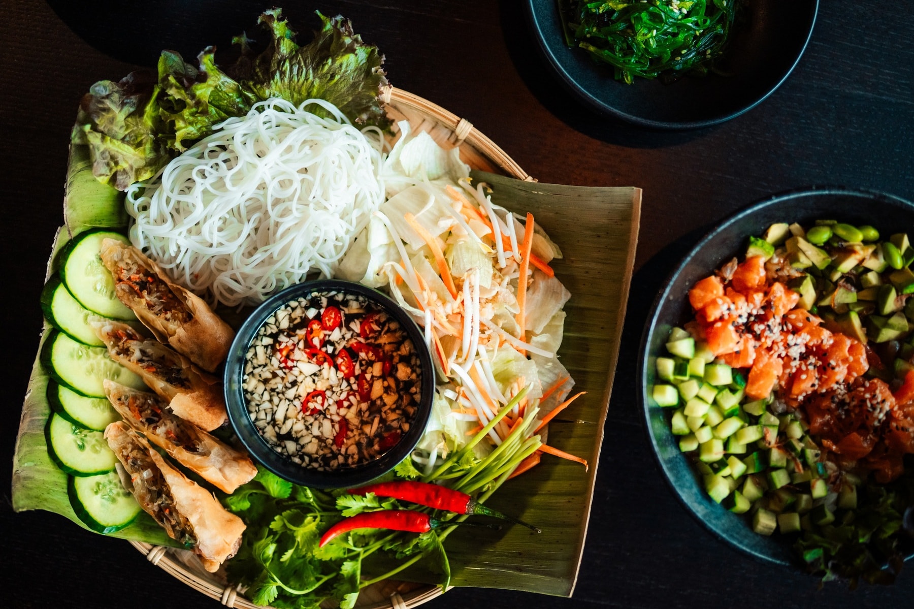 Vietnamesisches Bún Chả Giò mit frischem Gemüse und Dips, daneben Algensalat und Lachs-Poké Bowl.