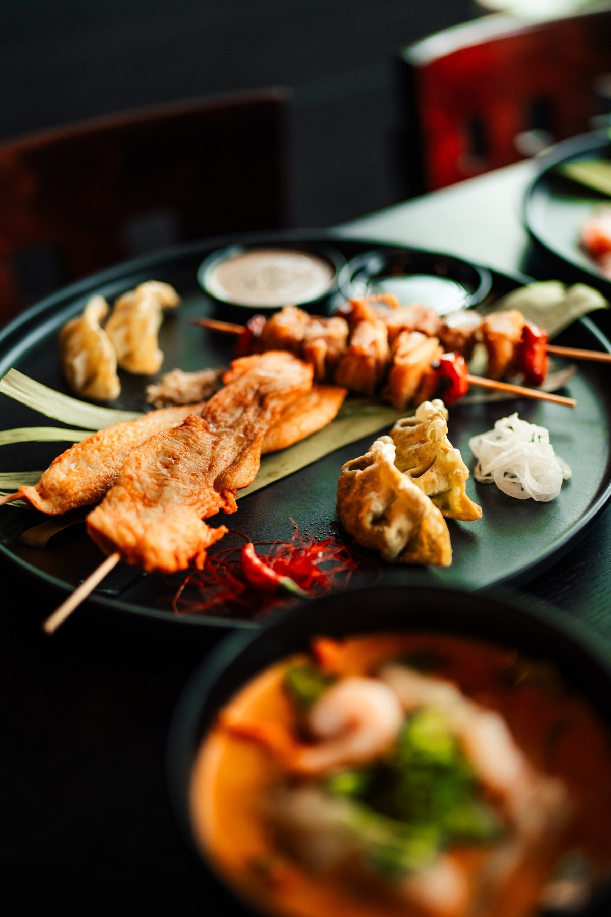 Gegrillte Spieße mit Gyoza und Tom Yum Suppe – asiatische Spezialitäten stilvoll serviert.