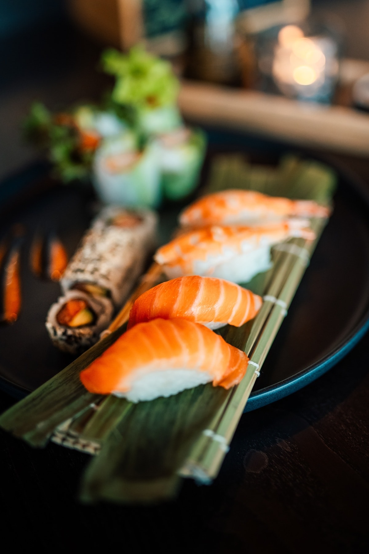 Lachs- und Garnelen-Nigiri mit Maki-Rollen und vietnamesischen Sommerrollen – stilvoll serviert auf Bambus und schwarzem Teller.